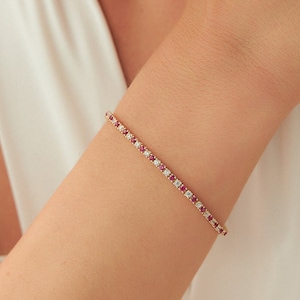 Pode incluir: Um delicado bracelete de ouro com pedras preciosas vermelhas e brancas alternadas. O bracelete é um design simples e elegante.