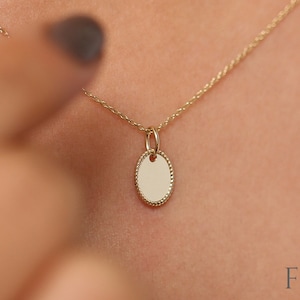 May include: A gold chain necklace with a small oval pendant. The pendant has a textured edge.