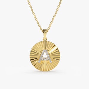 May include: A gold necklace with a round pendant featuring the letter 'A' set with small diamonds. The pendant has a sunburst design.