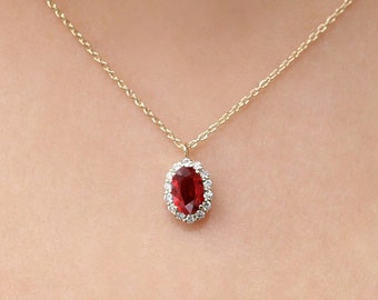 Puede incluir: Un collar de cadena de oro con un colgante de piedra ovalada roja rodeado de piedras pequeñas transparentes.