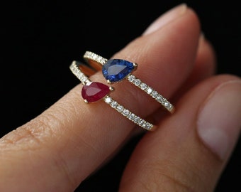 Puede incluir: Un anillo de oro con una montura de piedras preciosas rojas y azules. El anillo está engastado con pequeños diamantes alrededor de la banda.