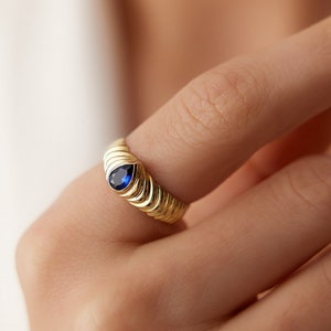 May include: A gold ring with a blue pear-shaped gemstone set in the center. The band is textured with a series of ridges.