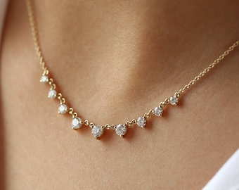 May include: A delicate gold necklace featuring a series of small, sparkling gemstones. The necklace is designed with a curved arrangement of evenly spaced stones, creating a subtle yet elegant look. The necklace is shown against a white shirt.