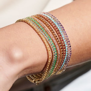May include: A set of gold bracelets with colourful gemstones. Each bracelet features a different colour of gemstones, including turquoise, pink, green, and red.