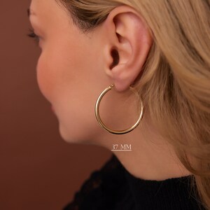 Puede incluir: Pendientes de aro de oro de 37 mm de di&aacute;metro. Los pendientes se muestran en la oreja de una modelo.