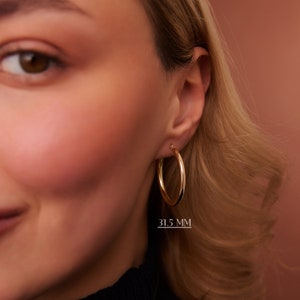 Puede incluir: Pendientes de aro de oro con un di&aacute;metro de 31,5 mm. Los pendientes se muestran en la oreja de una modelo.