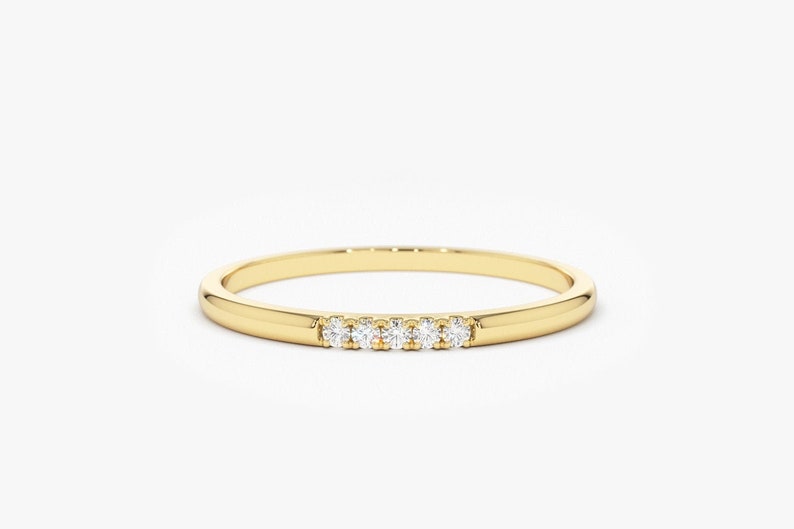 Op de afbeelding: Een dunne gouden band met een rij van vijf kleine diamanten die in het midden zijn gezet.