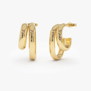 Puede incluir: Un par de pendientes de aro de oro con un diseño de doble aro. Los pendientes están hechos de un metal liso y brillante.