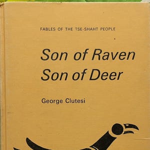 May include: A vintage book titled "Son of Raven Son of Deer" by George Clutesi. The cover is tan with black and red illustrations of a bird. The book is set against a green and white patterned background.