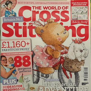 May include: A magazine cover for "The World of Cross Stitching" features a teddy bear and a dog riding a bicycle. The cover includes text such as "Britain's No.1", "88 gorgeous patterns", and "Let's go on an Adventure".