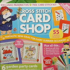 May include: A magazine cover featuring a colourful cross stitch card shop theme. The cover features a cartoon Paddington Bear, a bee, and various cross stitch patterns. The magazine title is "Cross Stitch Card Shop" and the text "55 Cards Inside!" is also visible. The magazine is promoting a free card stitch kit.