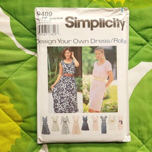 Peut inclure: Patron de couture Simplicity pour la création de robes. L'emballage présente des images de deux femmes portant des robes, ainsi que des illustrations de différents modèles de robes. Le texte sur l'emballage indique "Design Your Own Dress/Robe."
