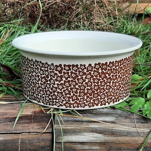 May include: A white ceramic bowl with a brown floral pattern. The bowl is round and has a wide rim.