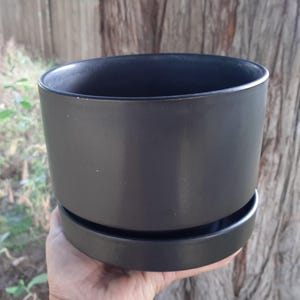 May include: A black ceramic planter with a matching saucer. The planter has a smooth, matt finish.