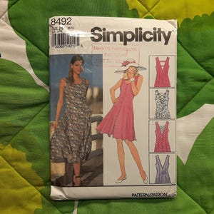 May include: A Simplicity sewing pattern envelope with illustrations of dresses. The envelope displays the number 8492 and the Simplicity logo. The dresses are in different styles, including a button-down dress and a floral print dress.