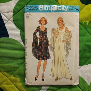 May include: A vintage Simplicity sewing pattern, number 7225, with illustrations of two dresses. The pattern cover displays the text "Simplicity" and "7225". The dresses are a cream-coloured gown and a black floral print dress.