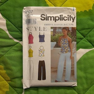 May include: A Simplicity sewing pattern packet featuring a woman in a floral halter top and white pants. The packet includes illustrations of various tops and pants styles. The packet is labeled with the number 9107 and the word "Simplicity".