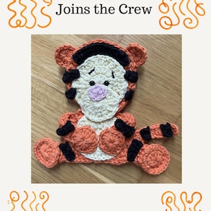 May include: A crocheted appliqué of the character Tigger, featuring orange and cream yarn with black stripes, a pink nose, and black eyes. The text Tigger Joins the Crew is displayed above the character, framed by orange swirling line patterns.