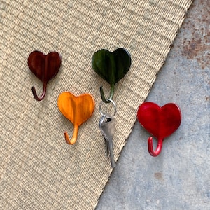 Puede incluir: Cuatro ganchos en forma de corazón en rojo, verde, naranja y marrón, con una llave plateada en un anillo que cuelga de uno de los ganchos.