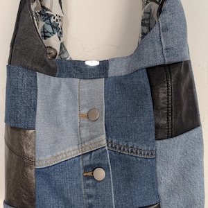 Peut inclure: Sac à bandoulière en denim patchwork, combinant des panneaux de denim bleu clair et foncé avec des accents de cuir noir et une doublure florale. Il comporte des boutons argentés et une base en denim roulé.