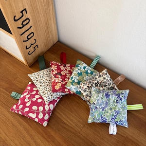 Puede incluir: Una colecci&oacute;n de seis saquitos de tela cuadrados y peque&ntilde;os con diversos estampados florales y de hojas en colores como rosa, rojo, azul cerceta, azul y blanco. Cada saquito tiene una peque&ntilde;a cinta de tela para colgar y uno incluye una etiqueta.