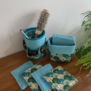 Puede incluir: Un conjunto de cuatro almohadillas desmaquillantes de tela con estampado azul y verde, un portacepillos de maquillaje de tela azul con un cepillo redondo para el cabello en el interior y una cesta de tela azul con un forro de tela azul y un exterior estampado en verde y dorado.