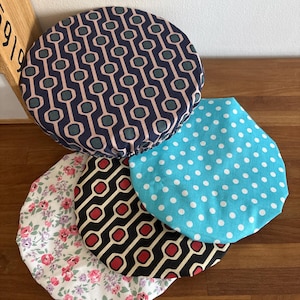 Peut inclure: Quatre couvercles de bol circulaires en tissu avec des bords élastiques. L'un présente un motif géométrique bleu marine, rose et sarcelle, un autre un imprimé à pois turquoise et blanc, un noir, crème et rouge, et un dernier un motif floral.
