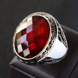 Peut inclure: Une bague en argent avec une grande pierre précieuse rouge facetée sertie dans un motif détaillé et orné.