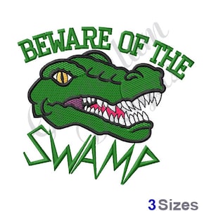Puede incluir: Cabeza de cocodrilo verde con dientes afilados y un ojo amarillo. El texto "Beware of the Swamp" está por encima de la cabeza del cocodrilo y la palabra "Swamp" está por debajo de la cabeza en una fuente estilizada.