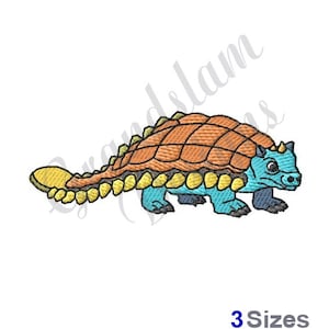 Puede incluir: Diseño de bordado de dinosaurio Ankylosaurus. El dinosaurio es azul con una concha marrón y amarilla. Tiene una cabeza pequeña con una espina en la parte superior.