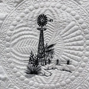 May include: White quilted textile featuring a black and white embroidered windmill scene. The design includes a windmill, plants, and a fence, set against a backdrop of intricate quilted patterns. The overall theme is a rustic, country aesthetic.