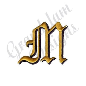 May include: An embroidered letter M in a gothic font style, featuring a metallic gold thread finish with a dark purple outline. The design is rendered with a textured stitch pattern, creating a raised appearance against a plain white background.