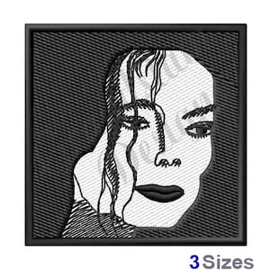 May include: Black and white embroidered patch of a person's face with a black background. The person's face is partially obscured by their hair.