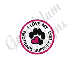 May include: A white circle with a pink border and the text "I Love My Emotional Support Dog" in black. A black paw print with a pink heart in the center is inside the circle.