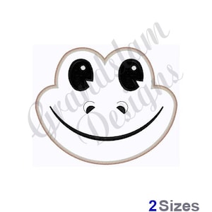 May include: A white frog face with black eyes and a wide smile. The frog face is outlined in a light brown color.