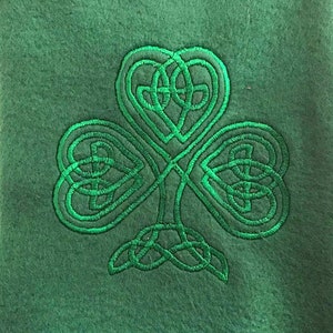 May include: A green shamrock embroidered on a green fabric background. The shamrock is a traditional Irish symbol.