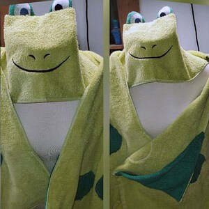 Può includere: Asciugamano con cappuccio verde con un viso di rana sul cappuccio. L'asciugamano è realizzato in morbido spugna e ha una combinazione di colori verde e blu.