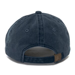 Puede incluir: Una gorra de b&eacute;isbol azul oscuro con una correa ajustable marr&oacute;n y un peque&ntilde;o logotipo en la parte posterior.