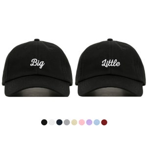 May include: Two black baseball caps with white embroidered text. One cap says "Big" and the other says "Little".