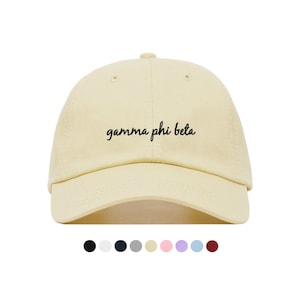 Op de afbeelding: Een lichtgele baseballpet met zwarte geborduurde tekst die "gamma phi beta" luidt.