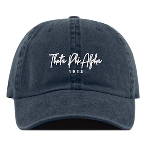 Puede incluir: Una gorra de béisbol de denim azul oscuro con texto bordado en blanco que dice "Theta Phi Alpha 1912".