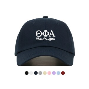 Puede incluir: Una gorra de béisbol azul marino con bordado blanco que dice "ΘΦΑ Theta Phi Alpha".
