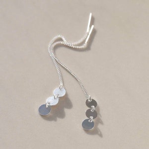 May include: A pair of silver dangle earrings with three circular charms on each earring. The charms are connected by a delicate chain.