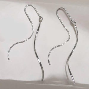 May include: A pair of silver-colored earrings. Each earring features a curved, elongated design with a delicate chain detail. The earrings have a hook closure and a flowing, elegant shape, suitable for everyday wear or special occasions.