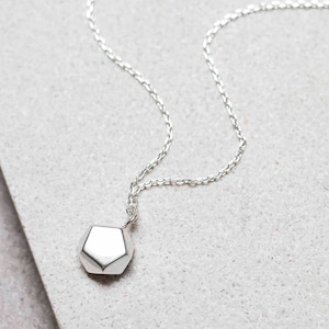 May include: A silver necklace with a geometric pendant. The pendant is a multifaceted shape, reflecting light. The chain is delicate and hangs on a neutral background. This necklace is a piece of jewelry.