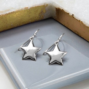 Pode incluir: Um par de brincos de estrela prateados. Os brincos são feitos de um metal liso e brilhante e têm um design simples e elegante.