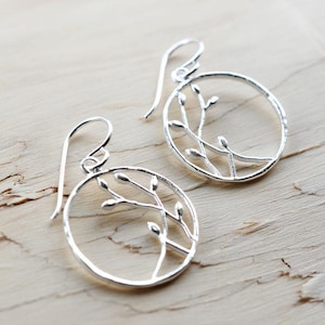 May include: Silver earrings with a circular design featuring a delicate branch with leaves.