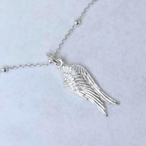 May include: A silver necklace with a detailed wing pendant. The wing is intricately designed with feather details and hangs from a delicate chain with small, round beads. The necklace is set against a white background.