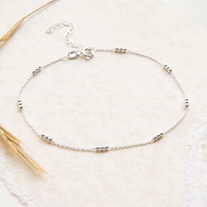 May include: A delicate silver anklet with a chain design and small beads. The anklet has a lobster clasp closure.