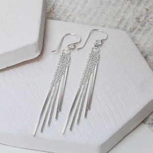 Peut inclure: Boucles d'oreilles pendantes en argent avec plusieurs fines chaînes et barres en argent suspendues au bas.